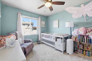 Bedroom with light carpet, a crib, and a ceiling fan