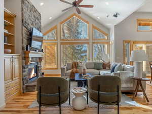 Living area featuring a stone fireplace, ceiling fan, light wood-style flooring, recessed lighting, and a high ceiling