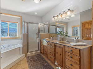Full bath with double vanity, a bath, light tile patterned floors, a shower stall, and healthy amount of natural light