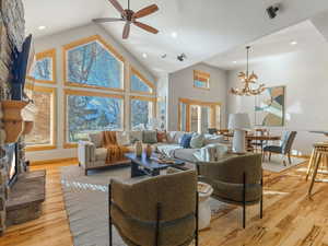 Living area featuring a stone fireplace, a high ceiling, a ceiling fan, suspended lighting, and light wood-style flooring