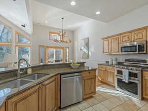 Kitchen with dark stone countertops, stainless steel appliances, suspended lighting, and light tile patterned floors