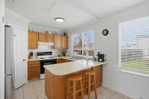 Kitchen with a kitchen breakfast bar, a peninsula, white range with electric stovetop, light countertops, and wood finish cabinetry