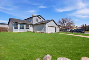 View of front of home with a front yard, driveway, a garage, a chimney, and roof with shingles
