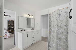 Ensuite bathroom with light colored carpet, double vanity, light tile patterned floors, ceiling fan, and a shower with curtain