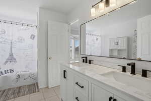 Full bathroom featuring double vanity, light tile patterned floors, and shower / tub combo