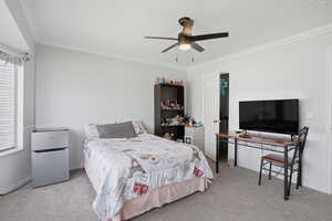 Bedroom with freestanding refrigerator, light colored carpet, crown molding, and a ceiling fan