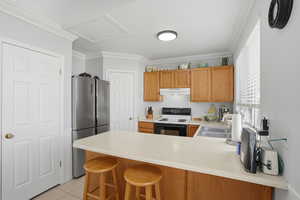 Kitchen featuring a peninsula, crown molding, light countertops, freestanding refrigerator, and range with electric cooktop