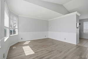 Empty room featuring light wood-type flooring, vaulted ceiling, and crown molding