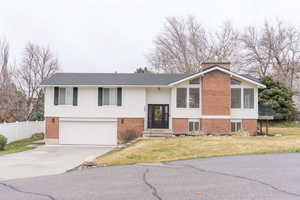 Split foyer home with concrete driveway, brick siding, and a chimney
