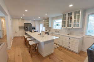 Kitchen featuring tasteful backsplash, a center island, glass insert cabinets, white cabinets, and light wood finished floors