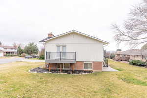 Back of house with a yard, a deck, a chimney, and brick siding