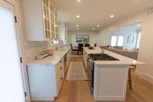 Kitchen with white cabinetry, stainless steel appliances, light wood-type flooring, glass fronted cabinets, and recessed lighting