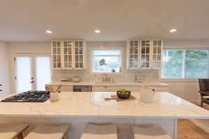 Kitchen with glass insert cabinets, white cabinets, light stone countertops, a breakfast bar, and a kitchen island