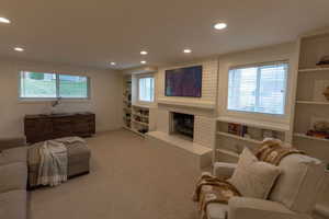 Carpeted living area with built in shelves, recessed lighting, and a brick fireplace