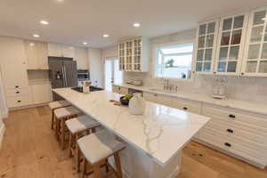 Kitchen with glass fronted cabinets, light wood-style flooring, a kitchen island, a kitchen breakfast bar, and white cabinetry