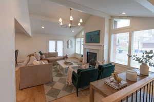 Living room featuring light wood finished floors, hanging lights, lofted ceiling, and a fireplace
