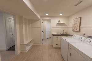 Laundry area with a wainscoted wall, light wood finished floors, washing machine and dryer, and recessed lighting