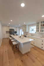 Kitchen featuring white cabinetry, glass insert cabinets, a spacious island, decorative backsplash, and light wood finished floors