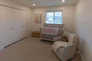 Bedroom with a nursery area, light carpet, a closet, and recessed lighting