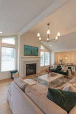 Living room with suspended lighting, light wood-style flooring, a glass covered fireplace, and vaulted ceiling