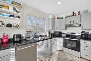 Kitchen with stainless steel appliances, gray cabinets, light tile patterned flooring, open shelves, and recessed lighting
