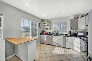 Kitchen featuring butcher block countertops, light tile patterned flooring, dishwashing machine, healthy amount of natural light, and recessed lighting