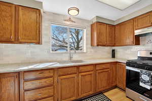 Kitchen with stainless steel gas stove, wood finish cabinetry, light quartz countertops, decorative backsplash, and light wood-style floors