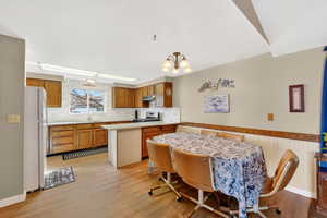 Kitchen featuring light countertops, wood finish cabinetry, freestanding refrigerator, a peninsula, and light wood-style floors