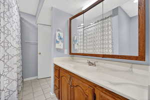 Full bathroom with curtained shower, vanity, light tile patterned floors, and a textured ceiling