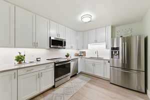 Kitchen featuring stainless steel appliances, white cabinets, and light wood-style floors