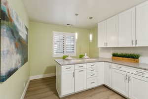 Kitchen featuring white cabinets, tasteful backsplash, light wood-type flooring, a peninsula, and decorative light fixtures