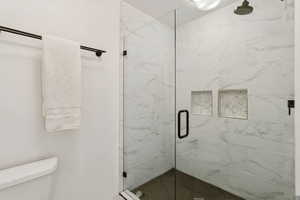 Full bathroom featuring a marble finish shower and toilet