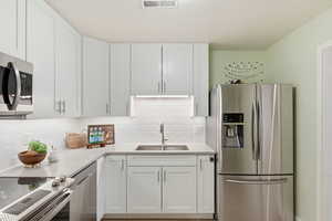 Kitchen featuring stainless steel appliances, white cabinetry, decorative backsplash, and light stone countertops