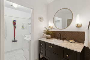 Bathroom with backsplash, vanity, washer and clothes dryer, and light marble finish floors