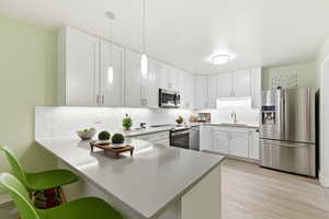 Kitchen with stainless steel appliances, a breakfast bar, a peninsula, white cabinetry, and light wood finished floors