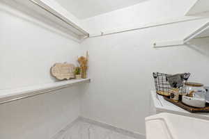 Walk in closet featuring washer and dryer and light marble finish flooring
