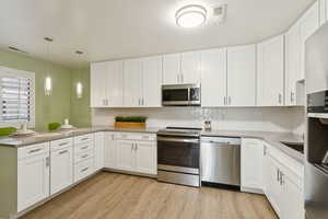 Kitchen featuring stainless steel appliances, white cabinets, backsplash, and light wood-style floors