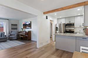 Kitchen with light stone counters, stainless steel appliances, beam ceiling, light wood finished floors, and gray cabinetry