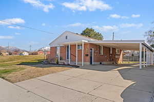 View of front of property featuring a carport, brick siding, driveway, and a porch