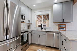 Kitchen featuring stainless steel appliances, light stone counters, light wood-style floors, recessed lighting, and gray cabinets