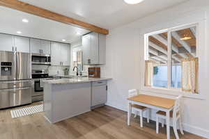 Kitchen with stainless steel appliances, light stone counters, beamed ceiling, light wood-style floors, and recessed lighting