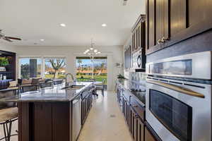 Kitchen with dark wood finish cabinets, stainless steel appliances, dark stone countertops, a kitchen bar, and an island with sink