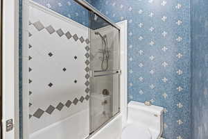 Full bathroom featuring wallpapered walls and combined bath / shower with glass door