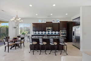 Kitchen featuring stainless steel appliances, a center island with sink, a chandelier, and dark wood finish cabinetry