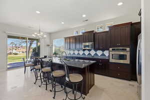 Kitchen with stainless steel appliances, a kitchen island with sink, dark stone counters, dark wood finish cabinetry, and a kitchen breakfast bar