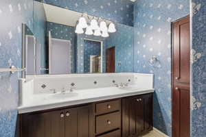Full bath with wallpapered walls, double vanity, and backsplash
