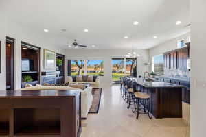 Kitchen featuring a kitchen island with sink, dark wood finish cabinetry, a kitchen breakfast bar, suspended lighting, and dark stone counters