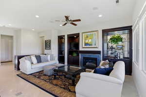 Living area with a ceiling fan, recessed lighting, a glass covered fireplace, and built in shelves
