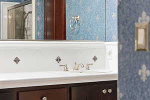 Bathroom with wallpapered walls, vanity, and tasteful backsplash