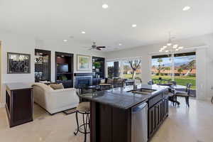 Kitchen with dark stone counters, suspended lighting, an island with sink, open floor plan, and a kitchen breakfast bar